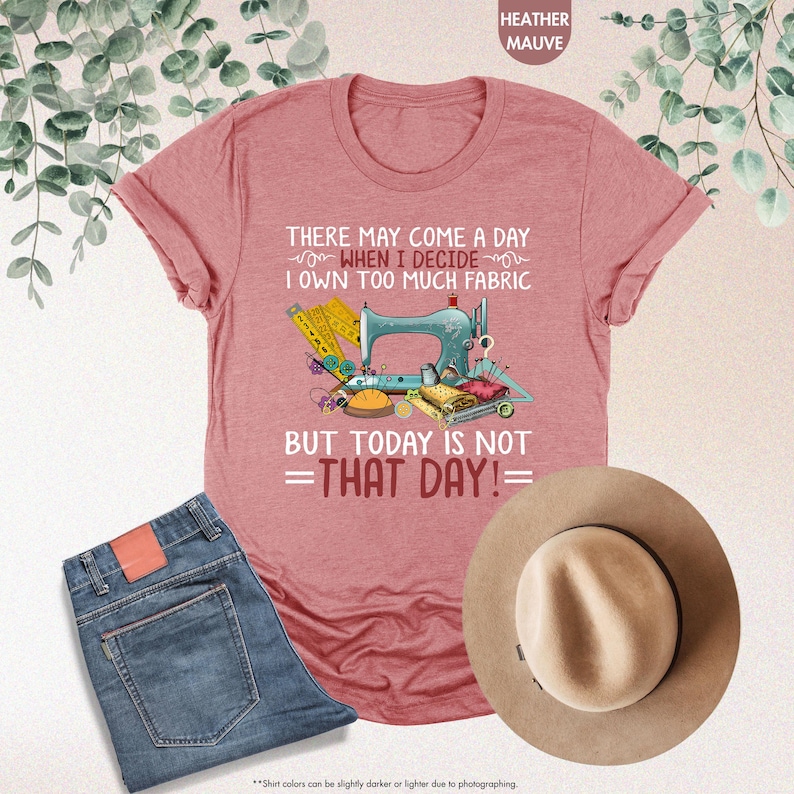 May include: Heather mauve t-shirt with a sewing machine and fabric design. The text on the shirt reads "There may come a day when I decide I own too much fabric but today is not that day!"