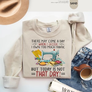 May include: A beige sweatshirt with a sewing machine graphic and the text "There may come a day when I decide I own too much fabric but today is not that day!"