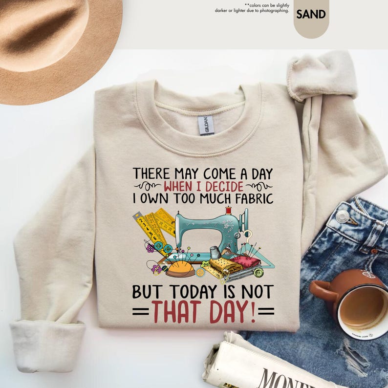 May include: A beige sweatshirt with a sewing machine graphic and the text "There may come a day when I decide I own too much fabric but today is not that day!"