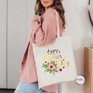 a woman holding a white tote bag that says happy mother's day