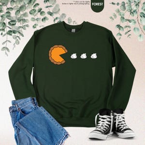 May include: A dark green sweatshirt with a graphic of a pumpkin pie slice eating three mini marshmallows. The text "FOREST" is in the top right corner of the image.