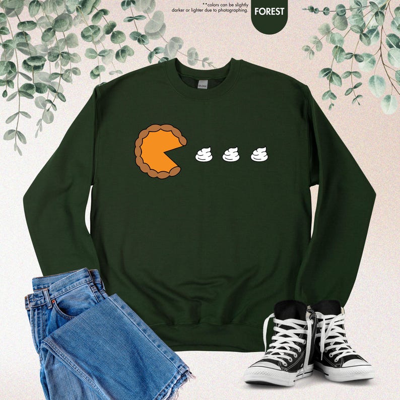 May include: A dark green sweatshirt with a graphic of a pumpkin pie slice eating three mini marshmallows. The text "FOREST" is in the top right corner of the image.