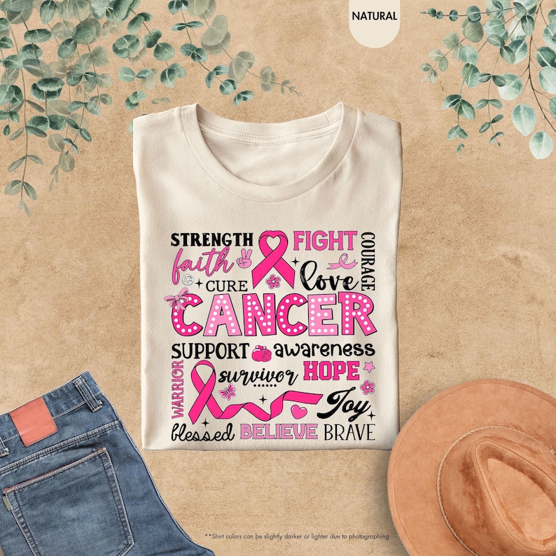 a t - shirt with a pink ribbon on it next to a cowboy hat