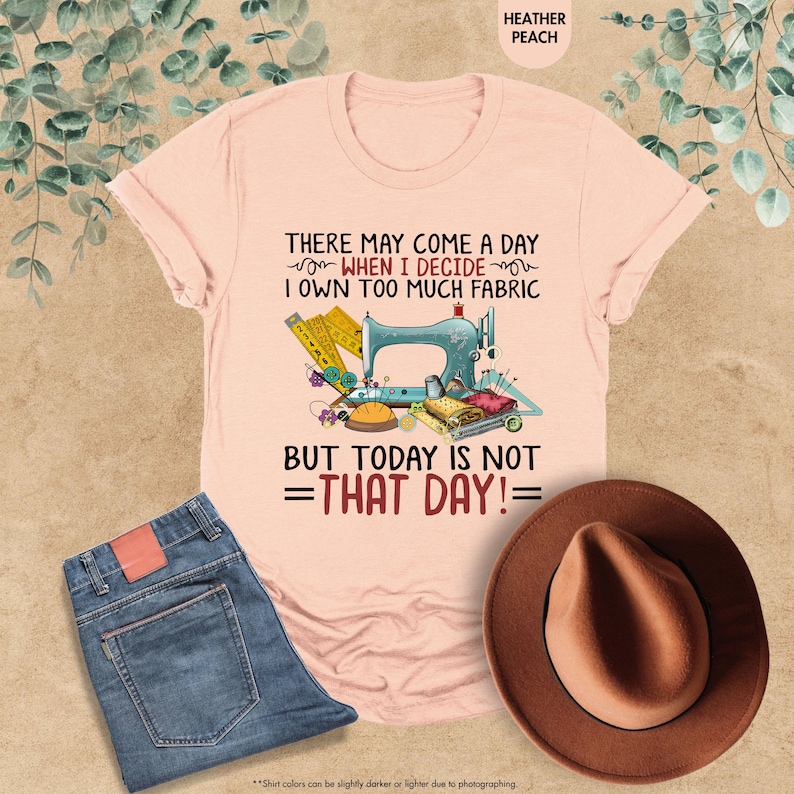 May include: A pink t-shirt with a sewing machine and sewing supplies graphic. The text on the shirt reads "There may come a day when I decide I own too much fabric but today is not =that day!="