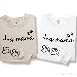 May include: Two long-sleeved sweatshirts, one sand-colored and one white, with the text "dog mama" in black script. Each shirt has paw prints and the names "Rex" and "Charlie" on the sleeve.