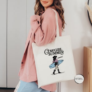 a woman holding a white tote bag with the words cowgirl summer on it