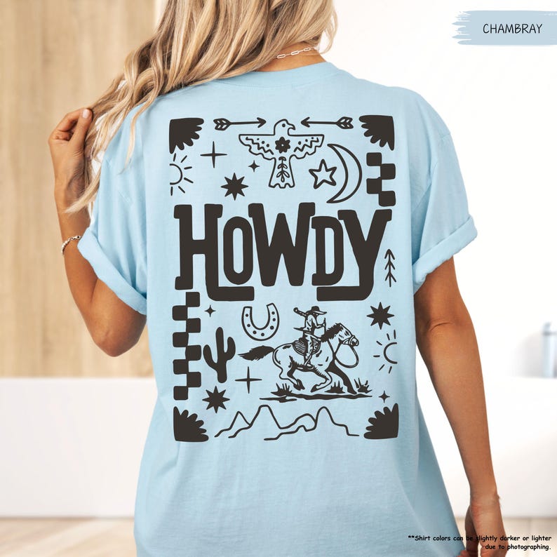 May include: A light blue t-shirt with a black graphic design featuring a cowboy riding a horse, a horseshoe, a cactus, and the word "HOWDY" in a western-style font.