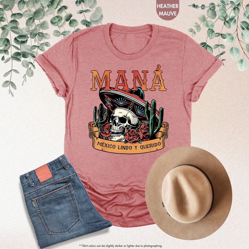 K&ouml;nnte beinhalten: Ein T-Shirt in der Farbe Heather Mauve mit einem Motiv eines Sch&auml;dels, der einen Sombrero tr&auml;gt, umgeben von Kakteen und Rosen. Der Text "MAN&Aacute;" und "M&Eacute;XICO LINDO Y QUERIDO" ist auf dem T-Shirt aufgedruckt.