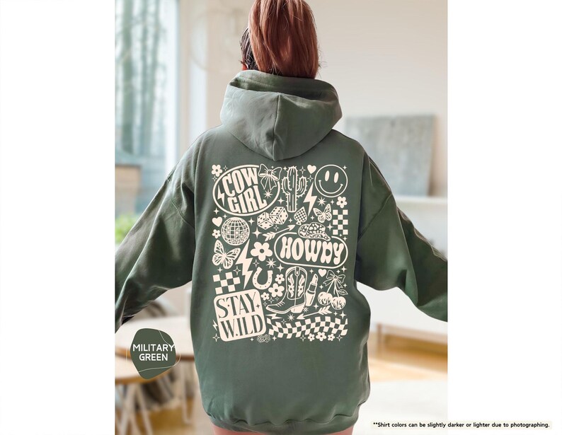K&ouml;nnte beinhalten: Milit&auml;rgr&uuml;ner Kapuzenpullover mit einem grafischen Design mit den Worten "Cow Girl", "Howdy" und "Stay Wild". Das Design umfasst einen Kaktus, Stiefel, ein Hufeisen, eine Discokugel, ein Smiley und andere wei&szlig;e Elemente.