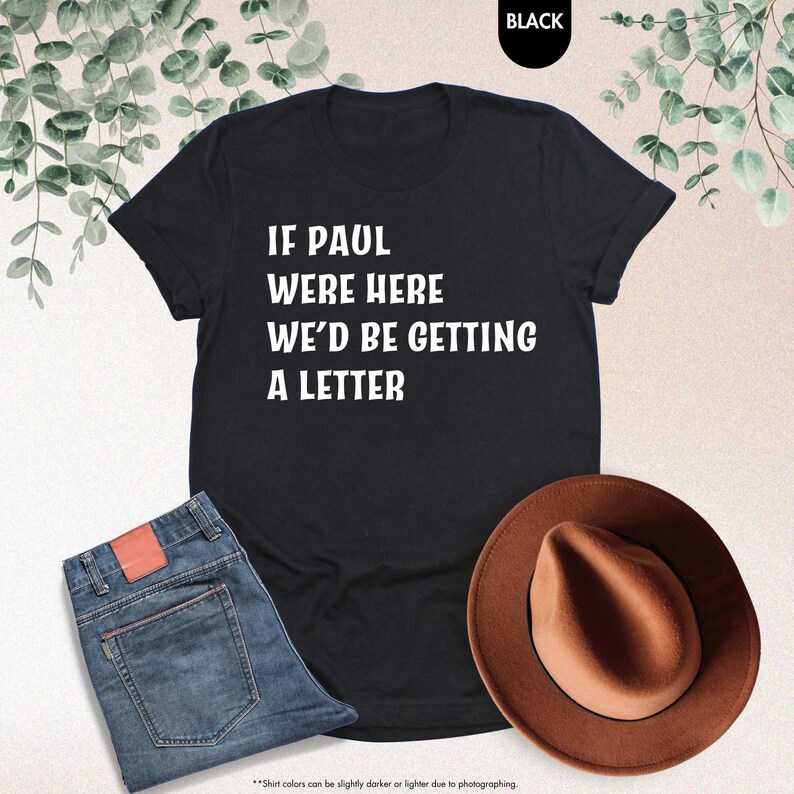 May include: Black t-shirt with the text "IF PAUL WERE HERE WE'D BE GETTING A LETTER" in white. The shirt is paired with blue jeans and a brown fedora hat. The word "BLACK" is in a black circle in the top right corner.
