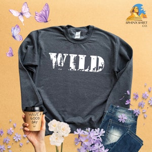 May include: A dark gray long-sleeve sweatshirt with the word "WILD" printed in white on the front. The letters are made up of images of trees, animals, and other nature-themed elements.