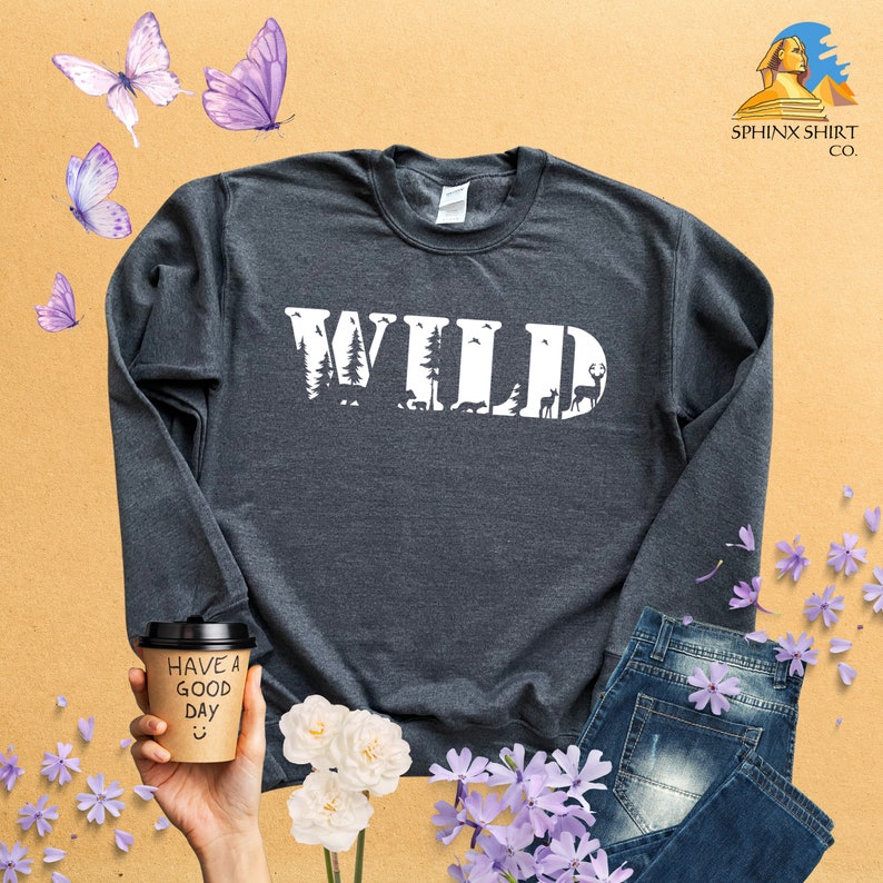 May include: A dark gray long-sleeve sweatshirt with the word "WILD" printed in white on the front. The letters are made up of images of trees, animals, and other nature-themed elements.