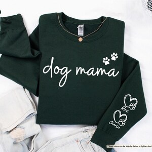May include: A dark green sweatshirt with the words "dog mama" in white script. Two paw prints are above the word "mama". The sleeve has two hearts with paw prints and the names "Rex" and "Charlie".