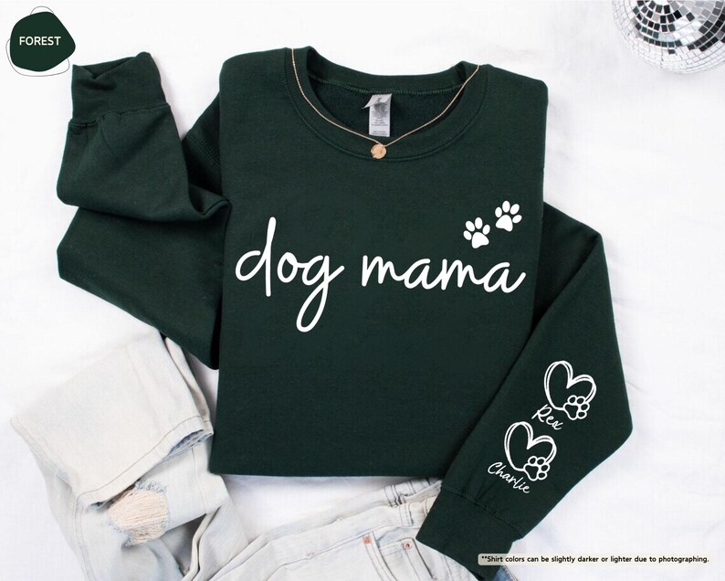 May include: A dark green sweatshirt with the words "dog mama" in white script. Two paw prints are above the word "mama". The sleeve has two hearts with paw prints and the names "Rex" and "Charlie".