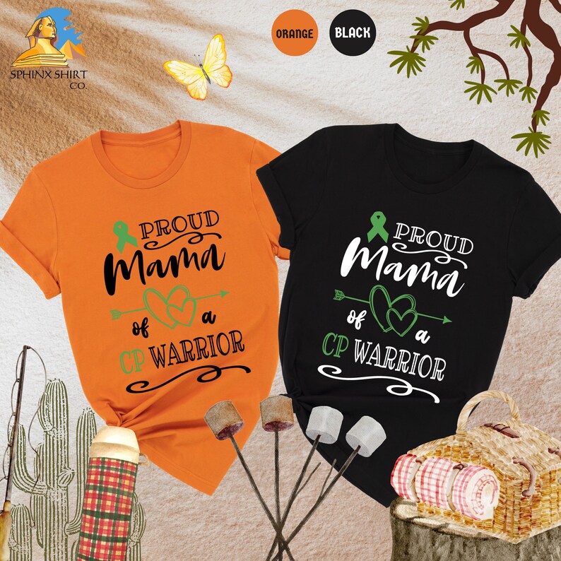 Op de afbeelding: Twee T-shirts, een oranje en een zwarte, met de tekst "Proud Mama of a CP Warrior" en een groen lint. De shirts worden getoond op een achtergrond met een picknickmand en een cactus.