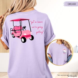 May include: Orchid-coloured t-shirt with a pink golf cart graphic and the text "get in losers we're going golfing." A smaller image on the right shows a golf ball with a bow.