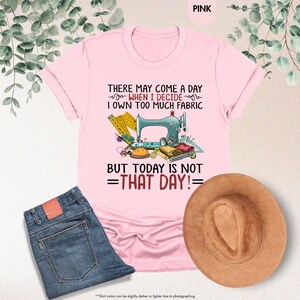 May include: Pink t-shirt with a sewing machine and sewing supplies graphic. The text on the shirt reads "There may come a day when I decide I own too much fabric but today is not that day!"