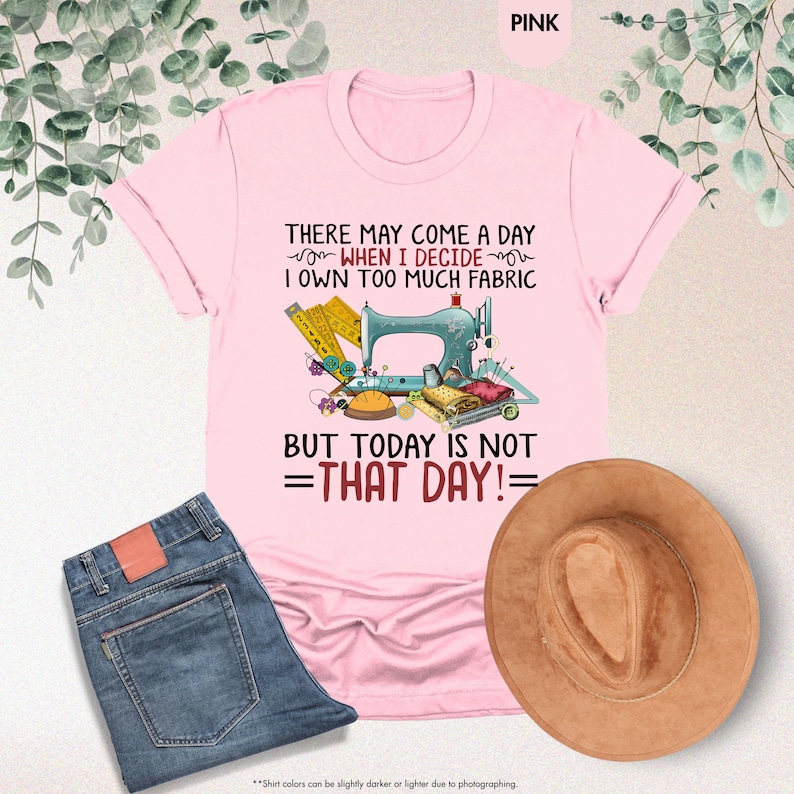 May include: Pink t-shirt with a sewing machine and sewing supplies graphic. The text on the shirt reads "There may come a day when I decide I own too much fabric but today is not that day!"