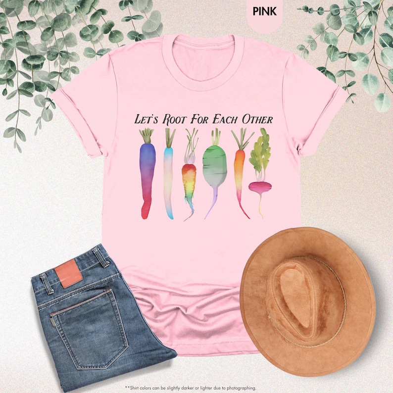 May include: Pink t-shirt with the text "Let's Root For Each Other" and a graphic of colorful vegetables, including carrots, radishes, and turnips.