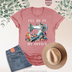 K&ouml;nnte beinhalten: Ein T-Shirt in der Farbe Heather Mauve mit einer wei&szlig;en Grafik einer N&auml;hmaschine und dem Text "I'll be in my office".