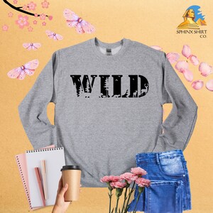 May include: Gray sweatshirt with the word "WILD" printed in black. The letters are outlined with a forest scene.