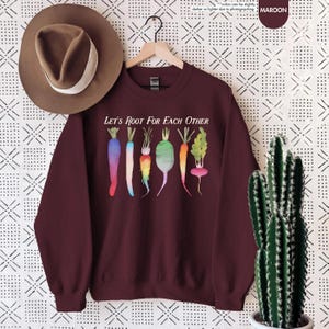 May include: Maroon sweatshirt with the text "Let's Root For Each Other" and a watercolor illustration of colorful carrots and radishes.