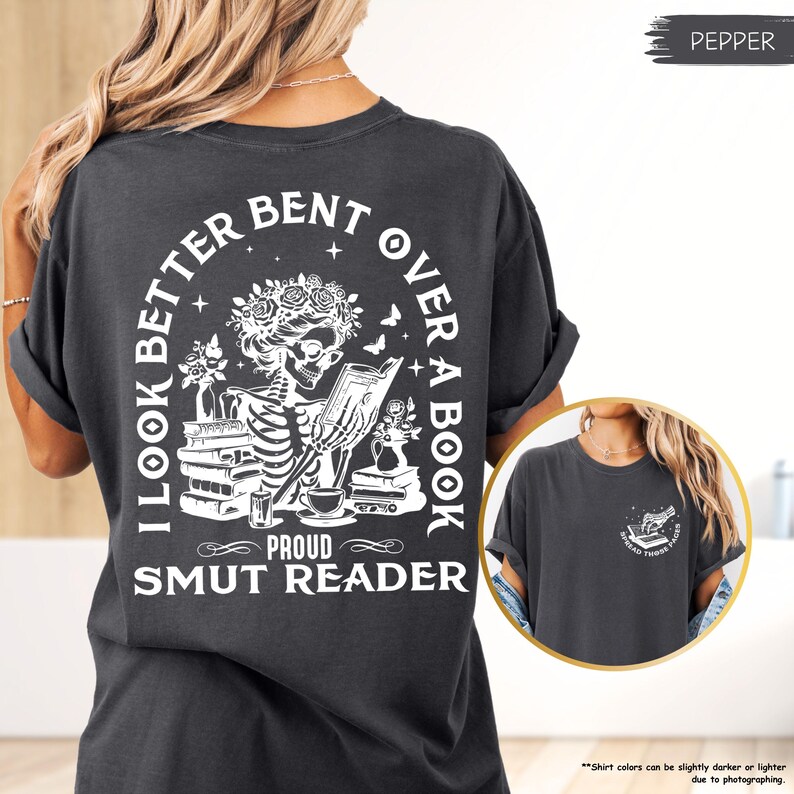 以下が含まれることがあります： 本を読んでいる骸骨の白いグラフィックが描かれた黒いTシャツ。シャツのテキストは「I look better bent over a book, Proud Smut Reader」です。