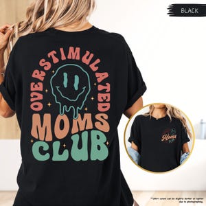 K&ouml;nnte beinhalten: Schwarzes T-Shirt mit dem Text "OVERSTIMULATED MOMS CLUB" in Retro-Schrift. Das Design beinhaltet ein schmelzendes Smiley-Gesicht. Das Shirt hat eine lockere Passform.