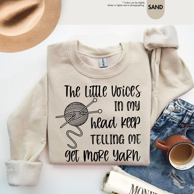 May include: A beige sweatshirt with the text "The Little Voices In My Head Keep Telling Me Get More Yarn" and a black and white illustration of a ball of yarn with knitting needles.