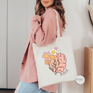 a woman holding a white bag with a picture of a brain and flowers on it