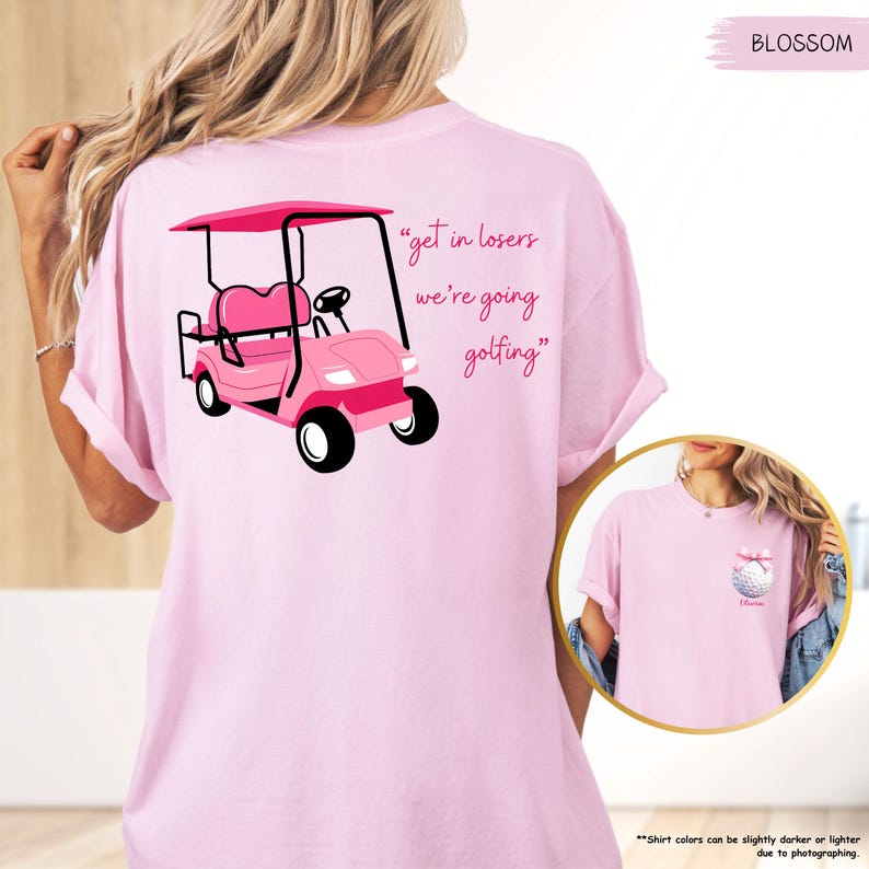 May include: Pale pink t-shirt featuring a pink golf cart illustration and the phrase "get in losers we're going golfing." The shirt also has a small golf ball graphic with a bow. The t-shirt is a light pink colour.