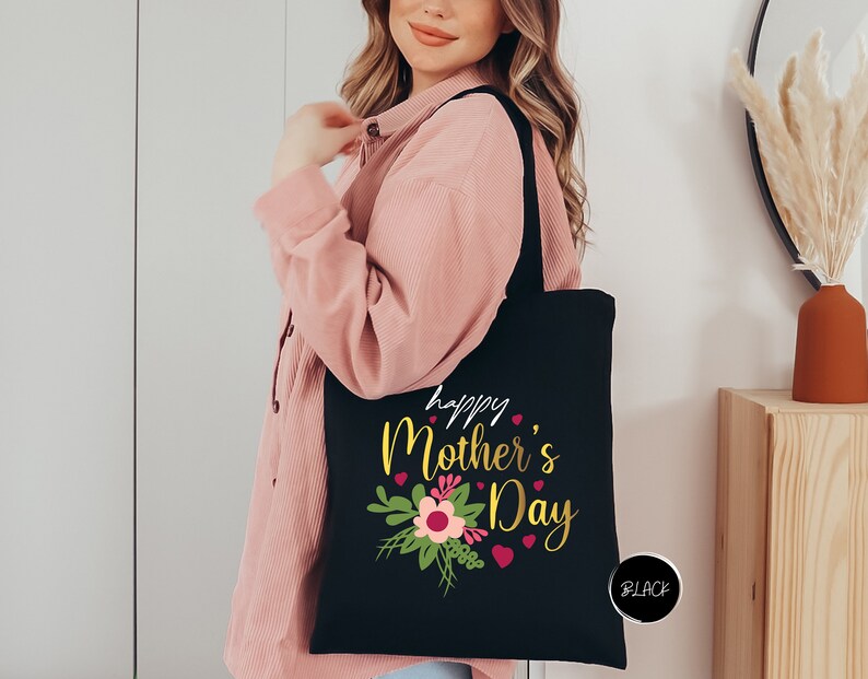 a woman holding a black tote bag that says happy mother's day