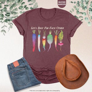 May include: A heather maroon t-shirt with the text "Let's Root For Each Other" and a graphic of colorful carrots and radishes.