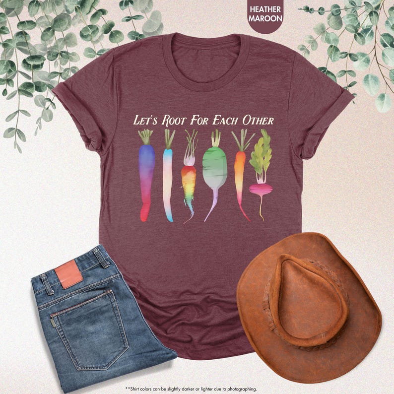 May include: A heather maroon t-shirt with the text "Let's Root For Each Other" and a graphic of colorful carrots and radishes.