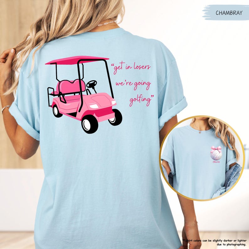 May include: Pale blue t-shirt with a pink golf cart illustration and the words "get in losers we're going golfing". The shirt has rolled sleeves and a small golf ball graphic on the front.