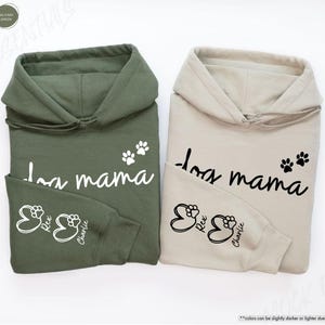 May include: Two hooded sweatshirts, one military green and one sand-colored, each featuring the text "dog mama" and paw prints. The sleeves display paw prints with the names "Rex" and "Charlie". The sweatshirts are made of a soft material.