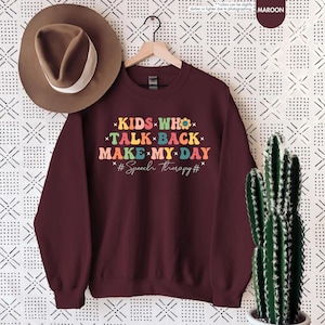 May include: Maroon sweatshirt with the text "KIDS WHO TALK BACK MAKE MY DAY #Speech therapy#" in colorful letters with flower accents.