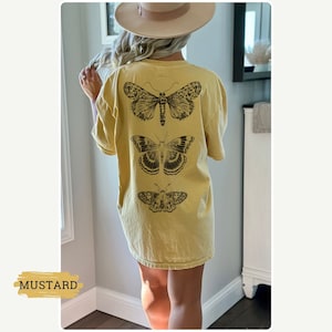 K&ouml;nnte beinhalten: Ein &uuml;bergro&szlig;es T-Shirt in Senfgelb mit einem Aufdruck von drei schwarzen Schmetterlingen auf der R&uuml;ckseite. Die Schmetterlinge sind vertikal angeordnet, wobei der gr&ouml;&szlig;te Schmetterling oben und der kleinste unten ist.