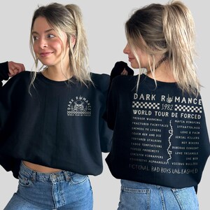 Puede incluir: Sudadera negra con el texto "DARK ROMANCE WORLD TOUR DE FORCED" y un gr&aacute;fico de calavera en la parte delantera. La parte trasera de la sudadera presenta una lista de frases y el texto "FICTIONAL BAD BOYS UNLEASHED".