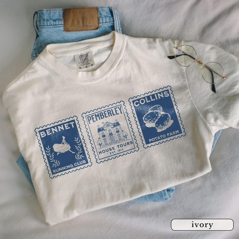 K&ouml;nnte beinhalten: Elfenbeinfarbenes T-Shirt mit drei blauen Briefmarken-Designs. Die Briefmarken zeigen die Aufschriften "Bennet Running Club", "Pemberley House Tours Est. 1813" und "Collins Potato Farm". Das Shirt wird mit hellblauen Jeans und einer Brille pr&auml;sentiert.