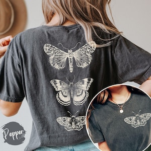 K&ouml;nnte beinhalten: Ein dunkelgraues T-Shirt mit einem Vintage-Schmetterlingsdesign, das auf der R&uuml;ckseite aufgedruckt ist. Das Schmetterlingsdesign zeigt drei Schmetterlinge in verschiedenen Gr&ouml;&szlig;en und Stilen.