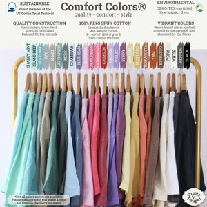 K&ouml;nnte beinhalten: Ein Gestell mit T-Shirts in verschiedenen Farben, darunter Kreideminze, Inselriff, Meeresschaum, Bucht, Khaki, Hellgr&uuml;n, Moos, Chambray, Jeansblau, Bl&uuml;te, Himbeere, Wassermelone, Scharlachrot, Orchidee, Violett, Beere, Banane, Senf, Terrakotta, Yam, Espresso, Elfenbein, Wei&szlig;, Pfeffer und Schwarz. Die T-Shirts bestehen aus 100 % Ringspinn-Baumwolle und sind in verschiedenen Gr&ouml;&szlig;en erh&auml;ltlich. Die T-Shirts sind mit dem Markennamen "Comfort Colors" und dem Text "Qualit&auml;t - Komfort - Style" gekennzeichnet.