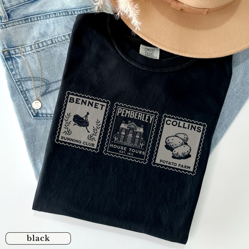 K&ouml;nnte beinhalten: Schwarzes T-Shirt mit drei grauen Briefmarken-Grafiken. Die Briefmarken lesen "BENNET RUNNING CLUB", "PEMBERLEY HOUSE TOURS EST. 1813" und "COLLINS POTATO FARM". Das Shirt liegt auf einem hellblauen Denim-Stoff.