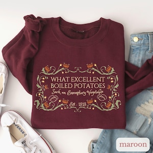 Puede incluir: Sudadera granate con el texto "WHAT EXCELLENT BOILED POTATOES Such an Exemplary Vegetable Est. 1813" en un marco decorativo. El dise&ntilde;o incluye ilustraciones de patatas y hojas. La palabra "maroon" es visible.