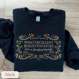 Puede incluir: Sudadera negra con un dise&ntilde;o decorativo y el texto "WHAT EXCELLENT BOILED POTATOES Such an Exemplary Vegetable Est. 1813". El dise&ntilde;o incluye elementos florales naranjas y verdes.