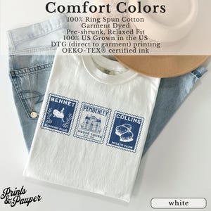 K&ouml;nnte beinhalten: Wei&szlig;es T-Shirt mit drei blauen Briefmarken-Designs. Die Briefmarken zeigen die W&ouml;rter "BENNET RUNNING CLUB", "PEMBERLEY HOUSE TOURS" und "COLLINS POTATO FARM". Das Shirt wird mit hellblauen Jeans und einem Hut kombiniert.