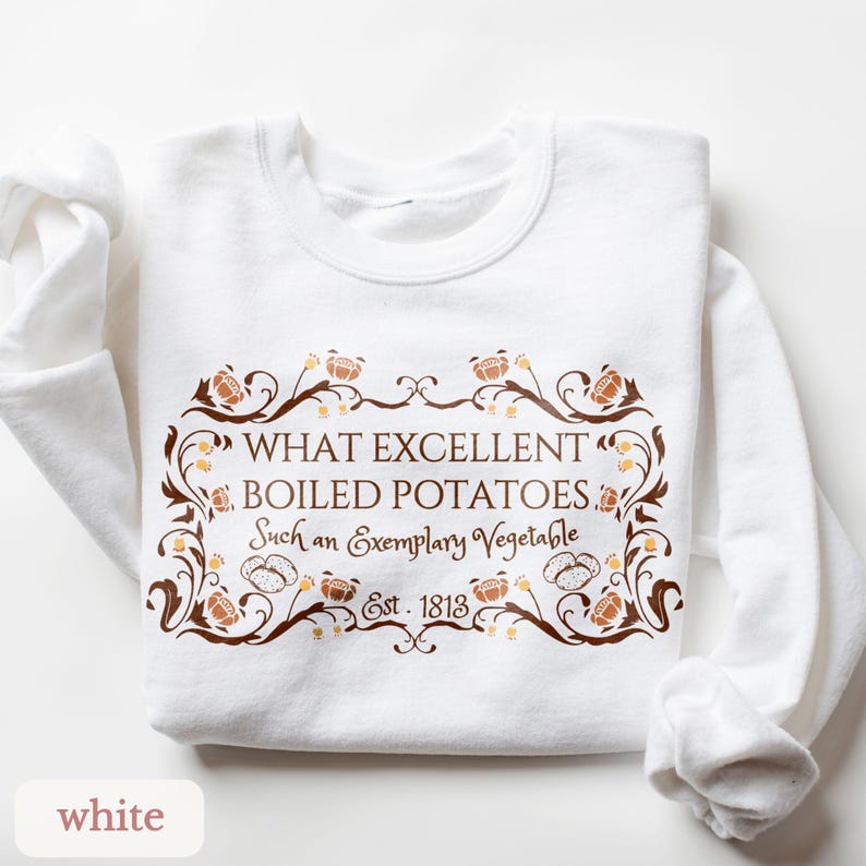 Puede incluir: Sudadera blanca con un dise&ntilde;o decorativo marr&oacute;n y dorado y el texto "WHAT EXCELLENT BOILED POTATOES. Such an Exemplary Vegetable. Est. 1813." La sudadera tiene mangas largas y cuello redondo.