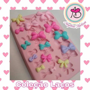 Pode incluir: Uma forma de silicone rosa preenchida com várias formas de laços em cores pastel, incluindo rosa, amarelo, azul e roxo. O texto "Coleção Laços" está na parte inferior, e um logotipo com o nome "Angelica Barbosa" está no canto superior direito.