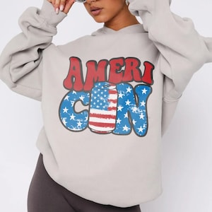 May include: A gray hoodie with a graphic print of a red, white, and blue can with stars and the text "AMERI CAN" in blue and red letters.