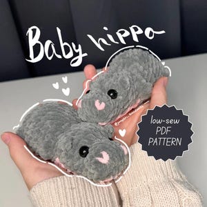May include: Two gray crocheted baby hippopotamus plushies with pink accents. The plushies are held in a person's hands. The text "Baby hippo" is written in black above the plushies. The text "low-sew PDF PATTERN" is written in white on a black circle below the plushies. The text "@pumpkin_head_works" is written in white on a black background below the plushies.